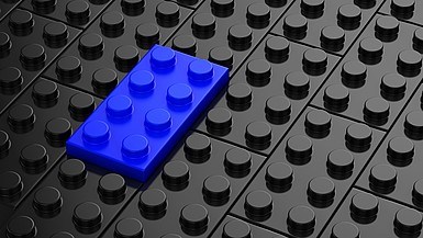 Blauer Legostein inmitten von schwarzen Legosteinen